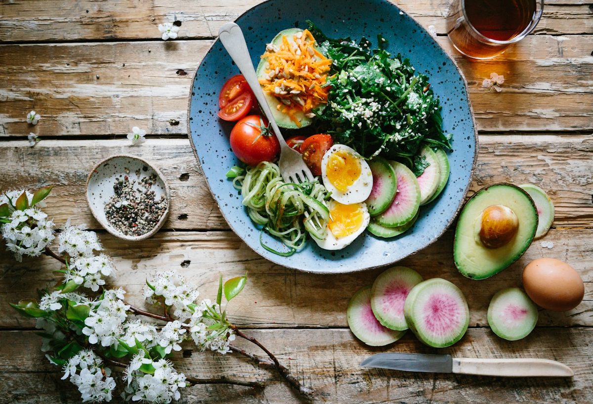 Bol de desayuno con huevo cocido, aguacate, tomate y verduras, junto a una taza de té