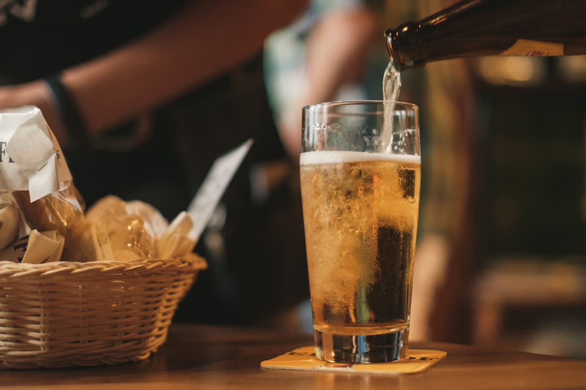 Cerveza sirviéndose en un vaso alto sobre la barra, junto a una cesta de pan
