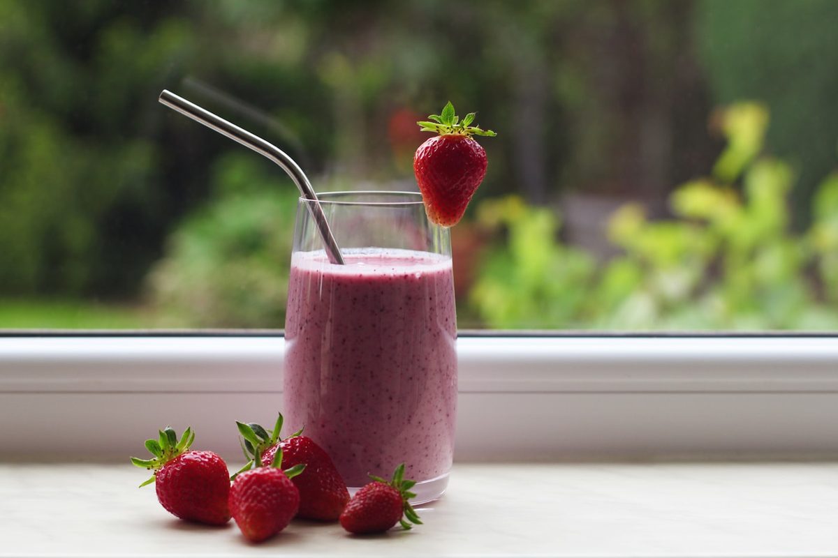 Batido de fresa en vaso alto con pajita y fresas frescas